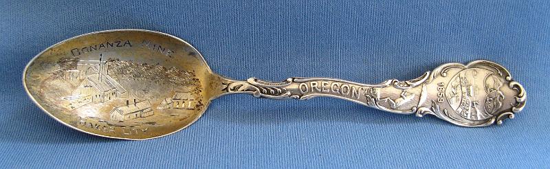 Souvenir Mining Spoon Bonanza Mine Baker City OR.JPG - SOUVENIR MINING SPOON BONANZA MINE ROBINSONVILLE OR - Sterling silver spoon with engraved mine scene in gold washed bowl, marked BONANZA MINE BAKER CITY, ca. 1895, marked Sterling with an S maker’s mark on reverse, made by the Shepard Mfg. Co. Melrose Highlands, MA 1893-1923, handle is marked OREGON with 1859 and crest at top, length 5 1/2 in. and weight 20.3 g,  [The Bonanza Gold Mine was the largest and probably the most valuable free gold mine in the Pacific Northwest in the 1890s.  It was located at the head waters of Burnt River at an elevation of 5,140 feet, about four miles southeast of Robinsonville in Baker County, Oregon, or approximately 40 miles west of Baker City. Discovered in 1877 by a pioneer prospector named Jack Haggard, it was worked by the original locators for two years, reducing the quartz and gold vein ores by the arrastra process. In 1879 the Bonanza Mining Co. purchased it, and erected a ten stamp mill. They continued operations, but failed to make a success of it, and finally closed down.  In 1892 the Geiser Company headed by Al Geiser purchased it, reopened the old works and had the mine and mill in continuous operation until it was sold in 1898, producing nearly $3 million in gold over that period as the heaviest producer in the state. The mine continued in operation till 1907 but little is known after that.  Most recently, a Canadian firm named the Marathon Gold Corp. of Toronto bought the Bonanza in 2012 from the Gazelle Land and Timber LLC of Canyon City with plans to conduct exploratory work.]